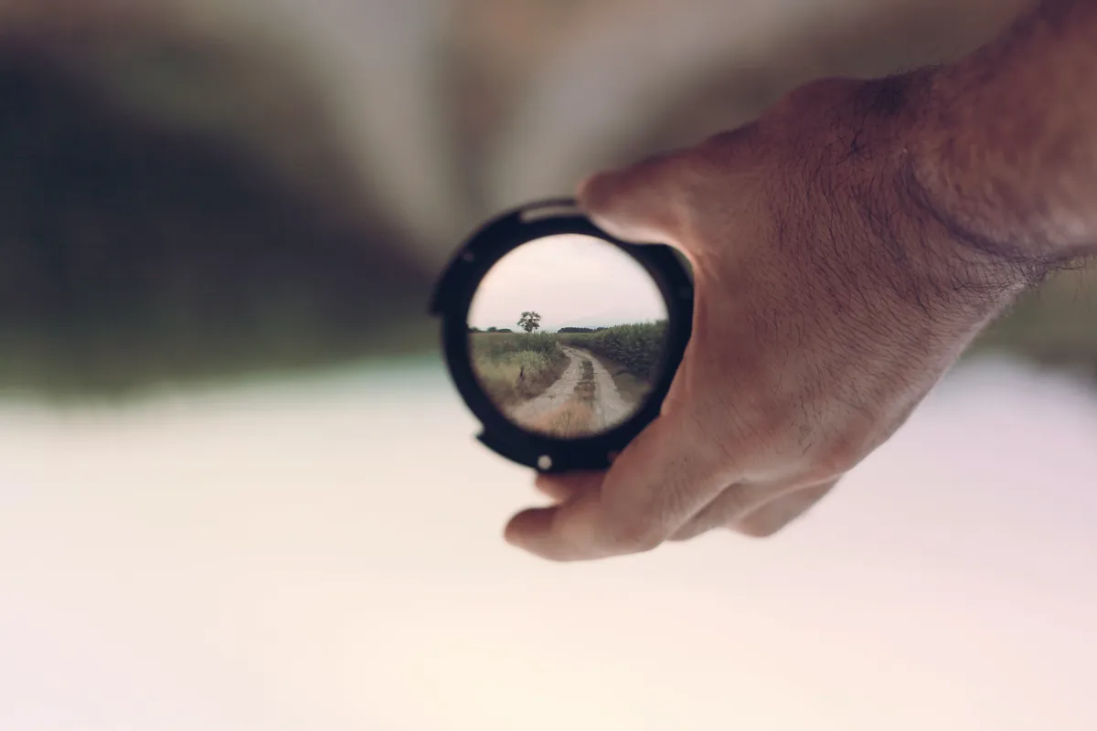 Hand holding a small lens that reflects a country road